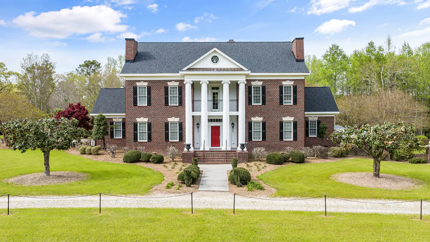 A large red-brick house with a white columned portico, set well back on a deep lawn.