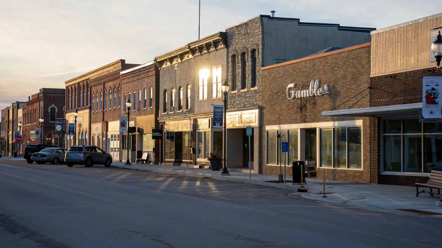 A downtown block of brick storefronts with street lamps, benches and angled parking.