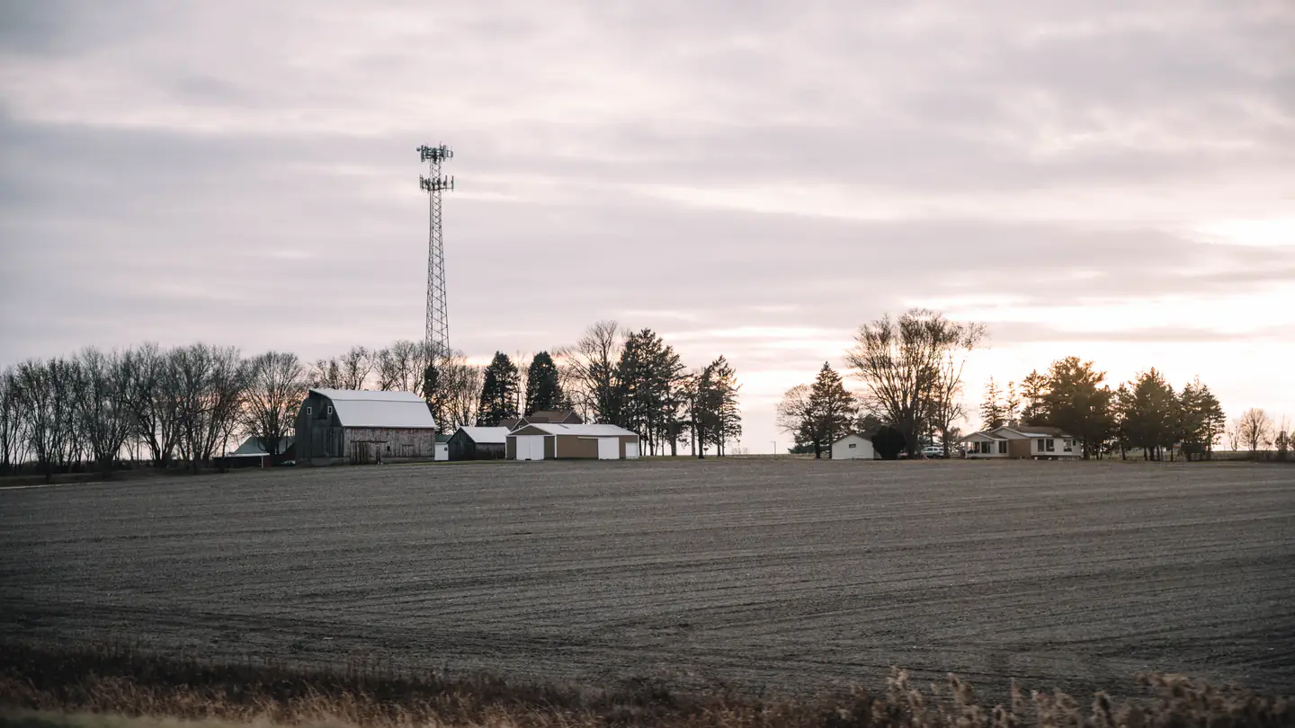 A plowed Illinois farm field running out to a low farmstead and a line of trees on the horizon.