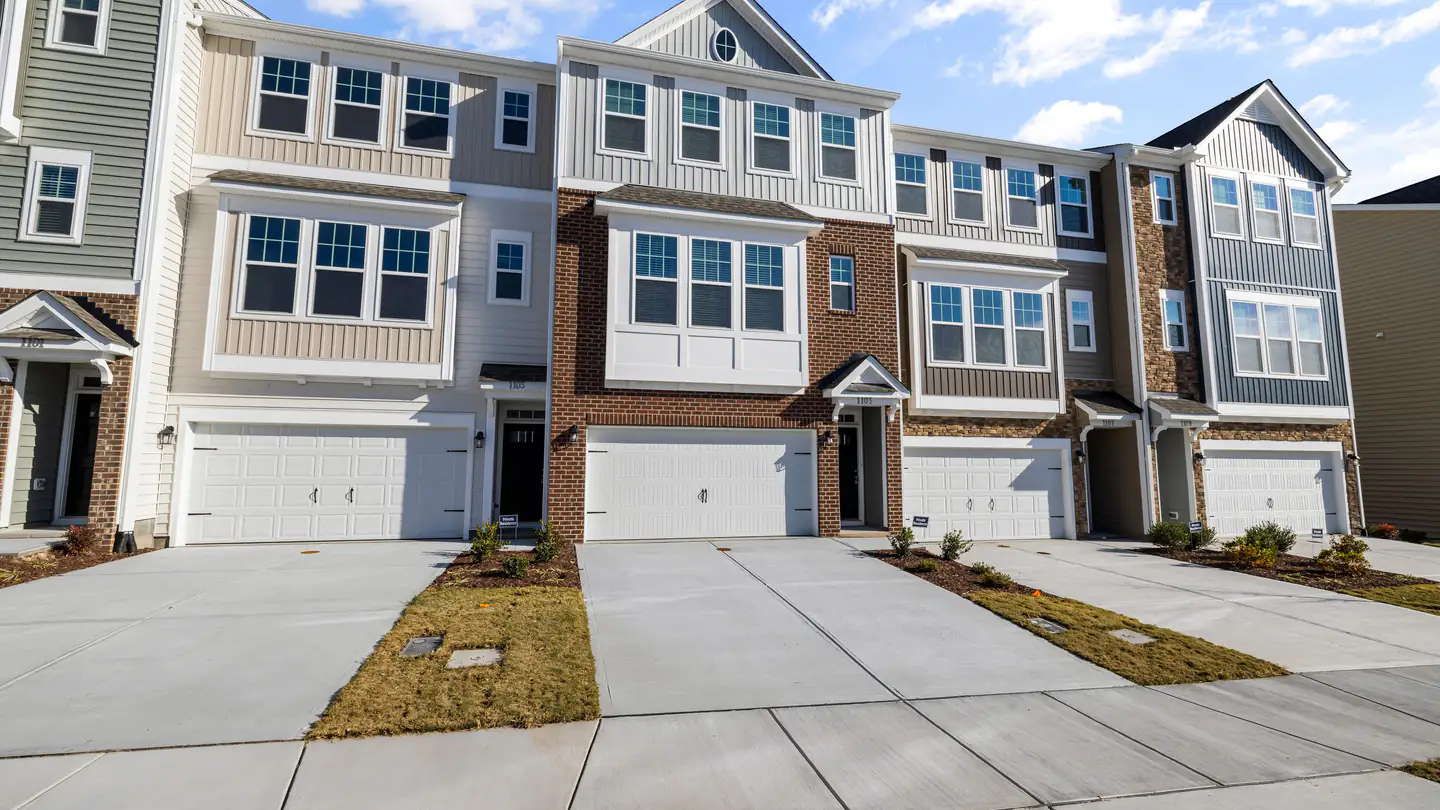 A row of newer three-story townhouses with attached garages and short driveways.
